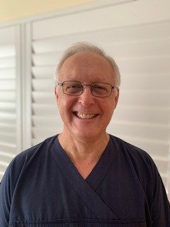 Dr Andrew Taylor smiles at the camera while wearing glasses and navy scrubs