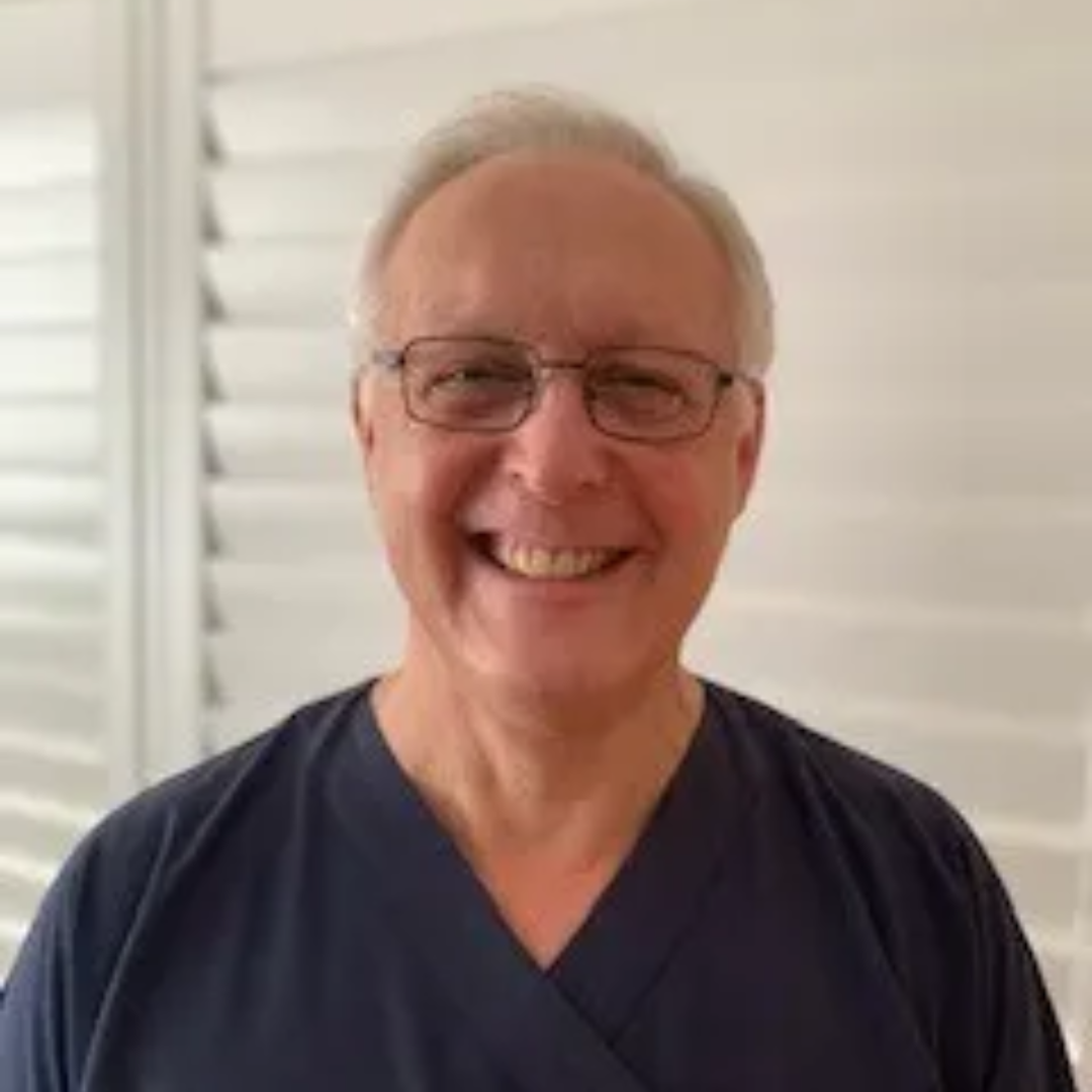 Dr Andrew Taylor smiles at the camera while wearing glasses and navy scrubs