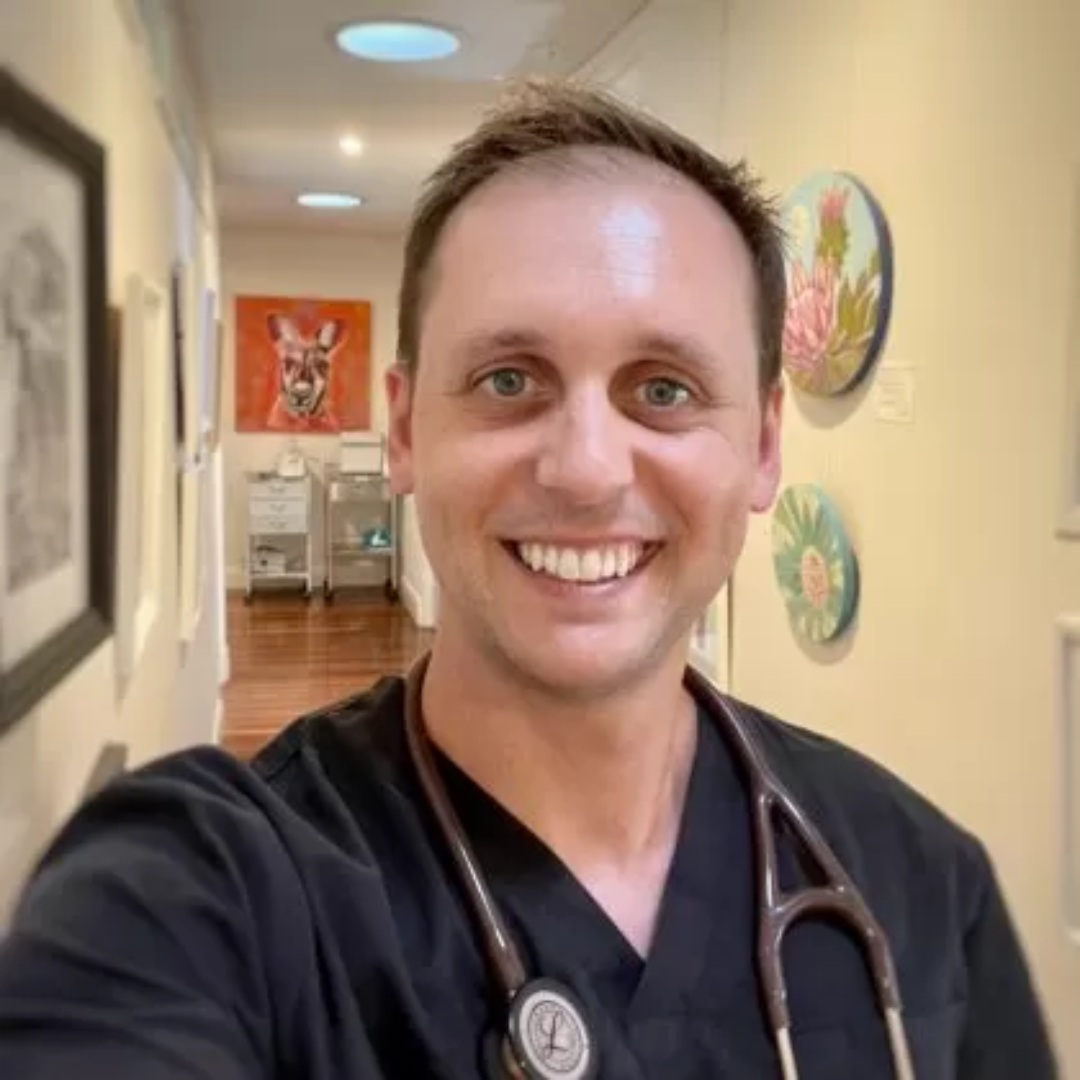 Dr Courtney Taylor smiles at the camera. He has a stethoscope around his neck and short dark hair