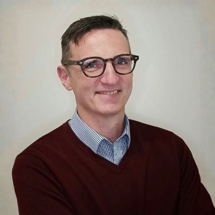 Dr Richard Tobin smiles at the camera while wearing glasses and a maroon jumper
